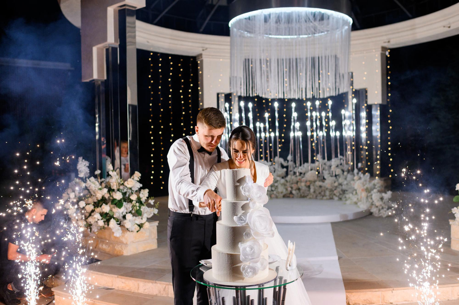 Vista frontal de um casal cortando um bolo de casamento, representando a importância da escolha do vestido para casamento à noite